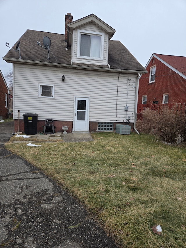 rear view of property featuring a lawn, central AC, a chimney, and a shingled roof