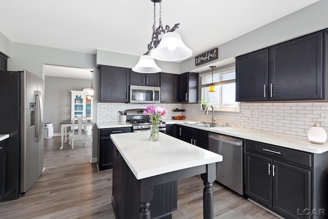 kitchen featuring light wood finished floors, light countertops, backsplash, appliances with stainless steel finishes, and a sink