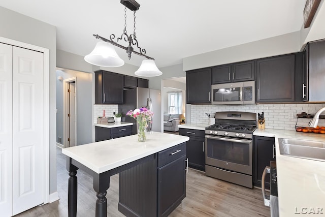 kitchen featuring light wood-style flooring, decorative light fixtures, stainless steel appliances, light countertops, and a sink