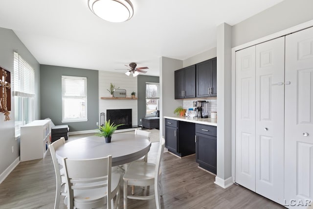 dining room with a ceiling fan, a fireplace, baseboards, and wood finished floors