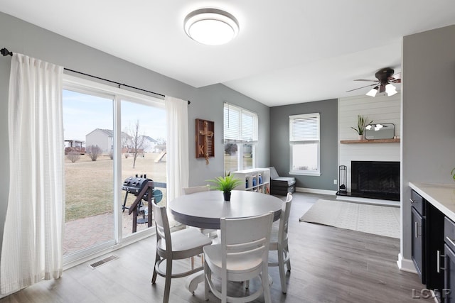 dining room with baseboards, visible vents, a ceiling fan, wood finished floors, and a fireplace