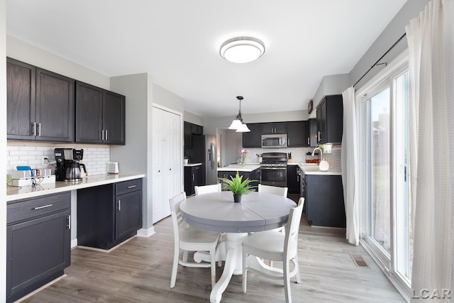 kitchen featuring light wood-style flooring, stainless steel appliances, a sink, light countertops, and backsplash