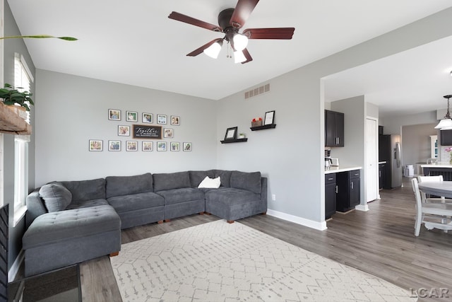 living room featuring baseboards, visible vents, ceiling fan, and wood finished floors