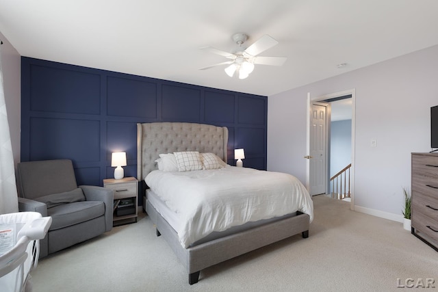 bedroom with ceiling fan, baseboards, light colored carpet, and a decorative wall