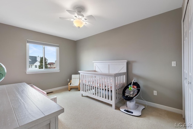 carpeted bedroom featuring a crib, ceiling fan, and baseboards