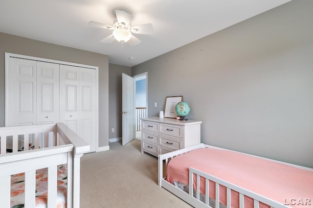 bedroom featuring baseboards, ceiling fan, a closet, and light colored carpet