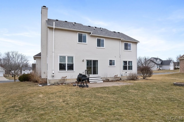 back of property with entry steps, a yard, a shingled roof, and a chimney