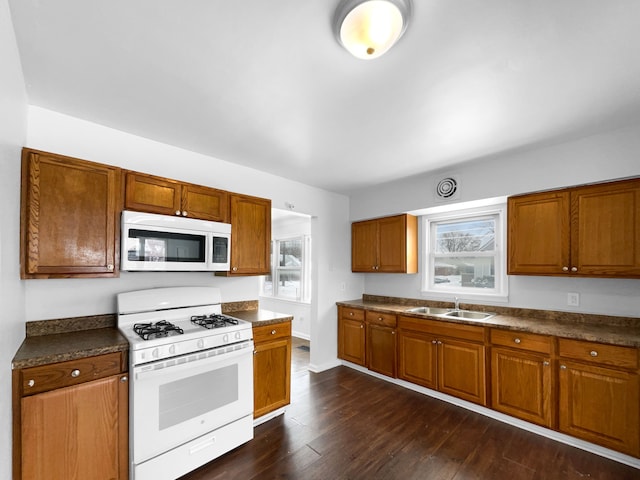 kitchen with white appliances, dark countertops, and a sink