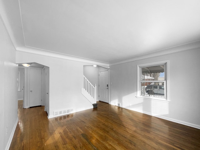 unfurnished living room featuring stairs, visible vents, arched walkways, and wood finished floors