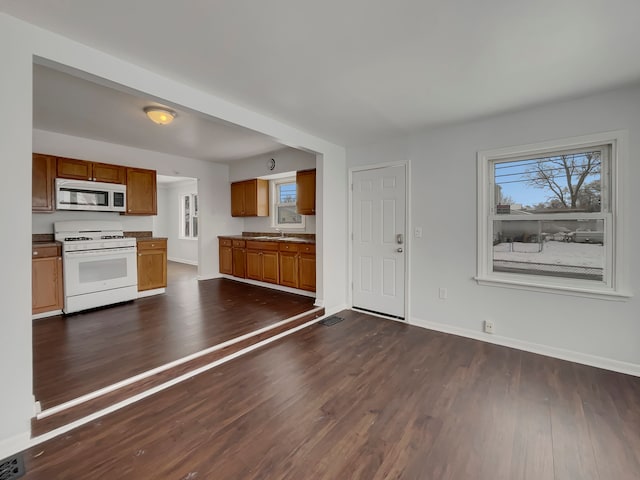 kitchen featuring brown cabinets, dark wood-type flooring, a sink, white appliances, and baseboards