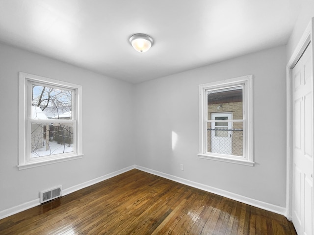 unfurnished bedroom with a closet, dark wood-style flooring, visible vents, and baseboards