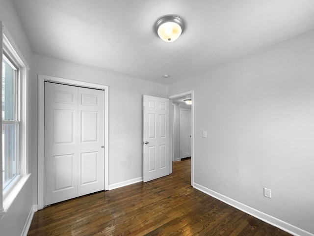 unfurnished bedroom with dark wood-style flooring, a closet, and baseboards