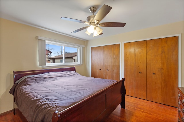 bedroom with multiple closets, a ceiling fan, baseboards, and wood finished floors