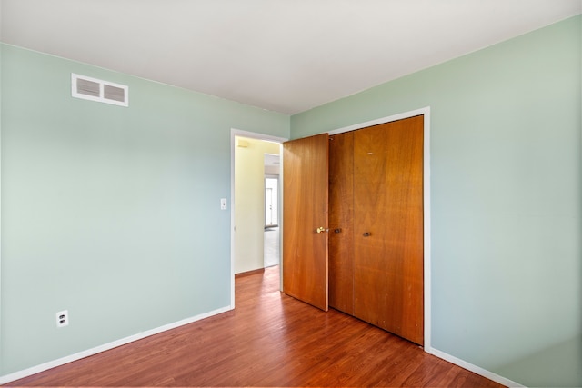 unfurnished bedroom featuring a closet, wood finished floors, visible vents, and baseboards