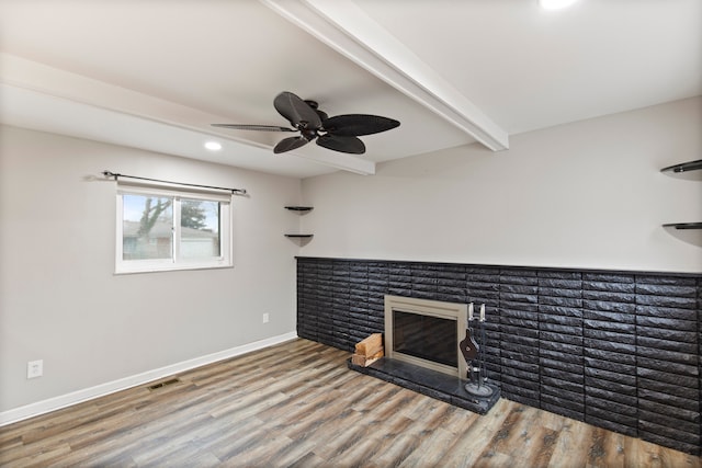 unfurnished living room featuring visible vents, a glass covered fireplace, wood finished floors, beamed ceiling, and baseboards