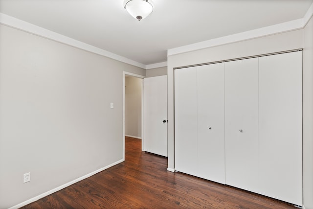 unfurnished bedroom with dark wood-style floors, a closet, ornamental molding, and baseboards