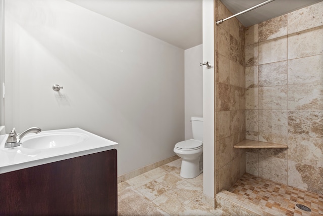 bathroom with tiled shower, vanity, toilet, and baseboards