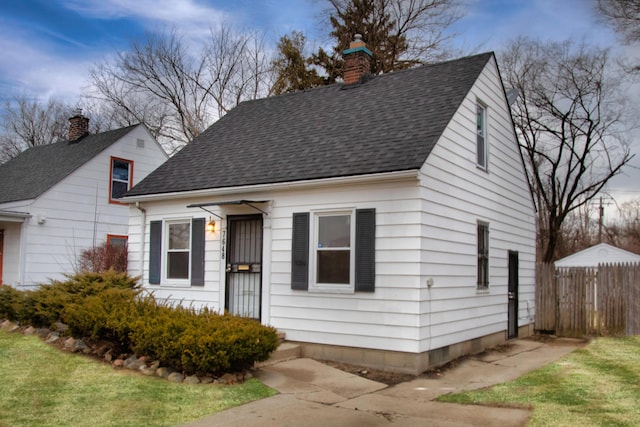 view of front of house featuring a shingled roof, a chimney, a front yard, and fence