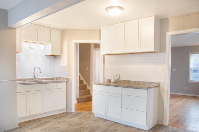 kitchen featuring light stone counters, light wood finished floors, decorative backsplash, white cabinets, and a sink