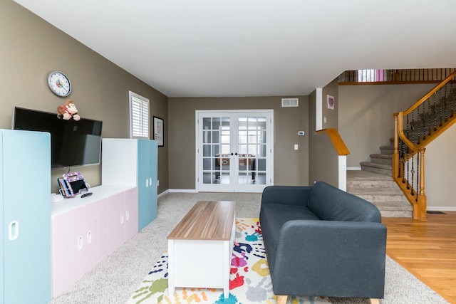 living room featuring baseboards, visible vents, stairs, french doors, and light wood-style floors