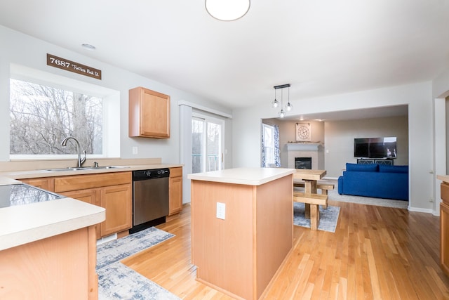 kitchen featuring a fireplace, light countertops, stainless steel dishwasher, open floor plan, and a sink