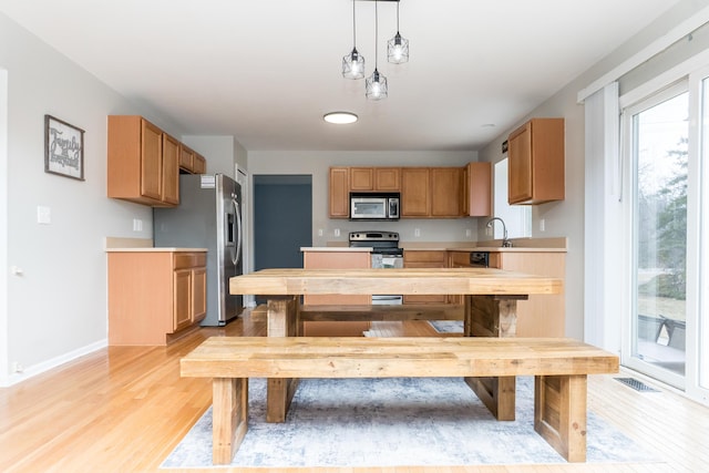 kitchen with light countertops, hanging light fixtures, appliances with stainless steel finishes, a sink, and light wood-type flooring