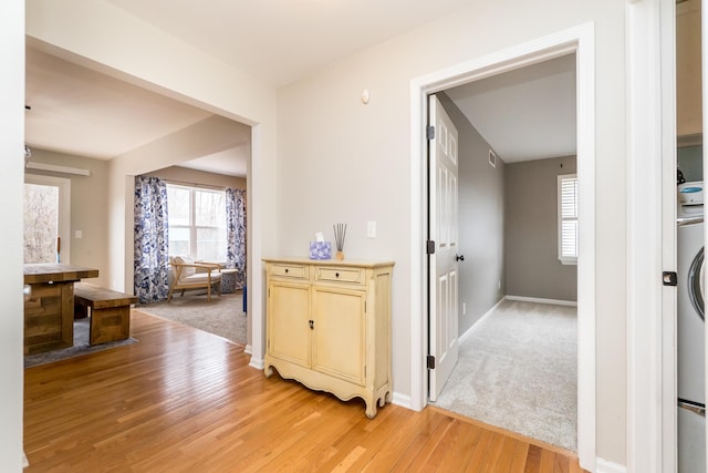 hall with baseboards, light colored carpet, and light wood-style floors