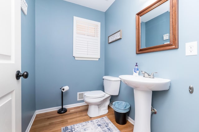 half bath with toilet, baseboards, visible vents, and wood finished floors