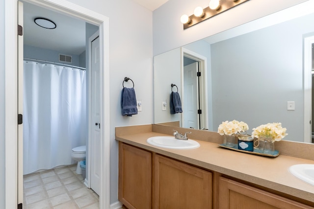 full bathroom with toilet, double vanity, a sink, and visible vents