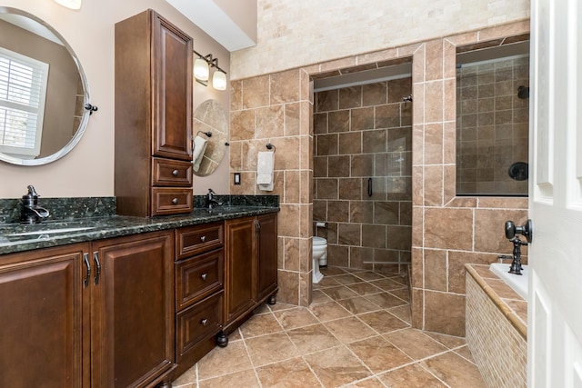 full bathroom featuring toilet, double vanity, a tile shower, and a sink