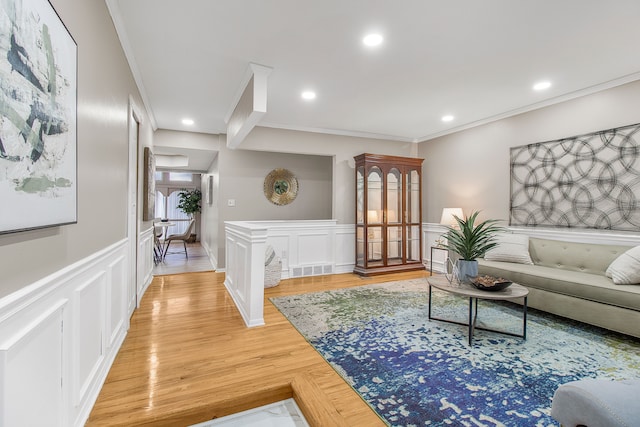 living room with light wood-style flooring, recessed lighting, a decorative wall, ornamental molding, and wainscoting