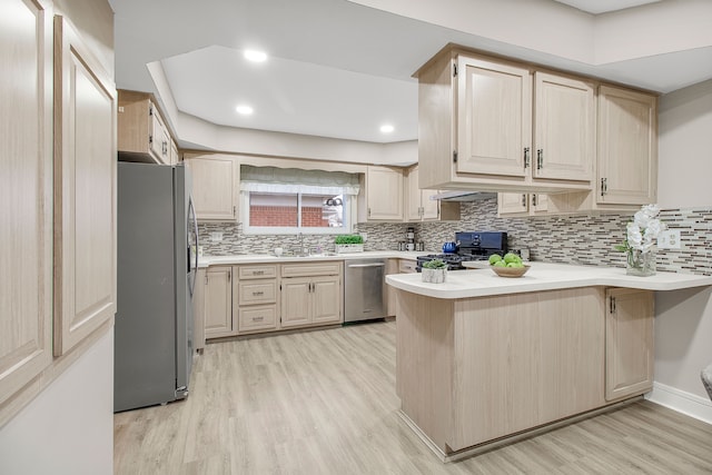 kitchen featuring light wood finished floors, appliances with stainless steel finishes, a peninsula, light countertops, and light brown cabinetry