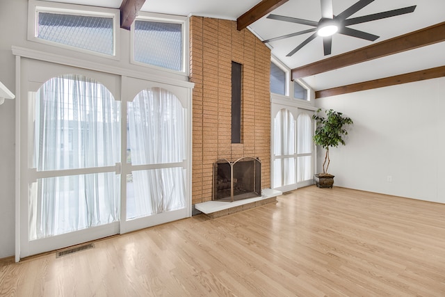 unfurnished living room with visible vents, a ceiling fan, wood finished floors, beamed ceiling, and a brick fireplace