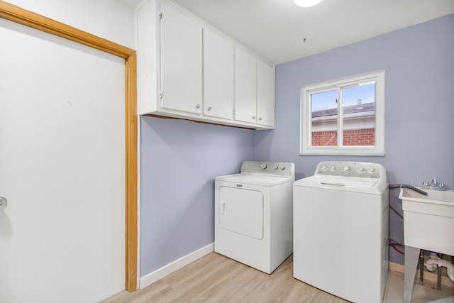 clothes washing area featuring cabinet space, light wood-style floors, washing machine and dryer, a sink, and baseboards