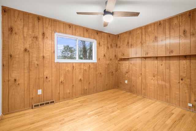 spare room featuring wood walls, ceiling fan, visible vents, and wood finished floors