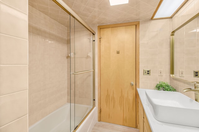 bathroom with enclosed tub / shower combo, wood finished floors, tile walls, and vanity