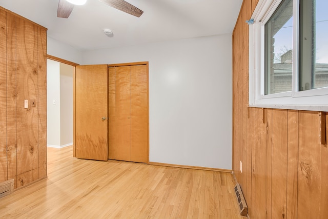 unfurnished bedroom with baseboards, visible vents, wood walls, light wood-style floors, and a closet