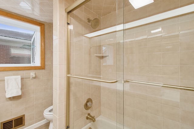 bathroom featuring toilet, bath / shower combo with glass door, and visible vents