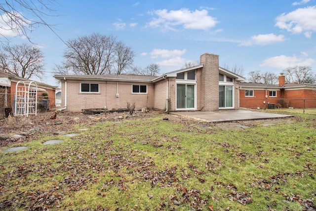 back of house featuring a lawn, a patio, a chimney, fence, and brick siding