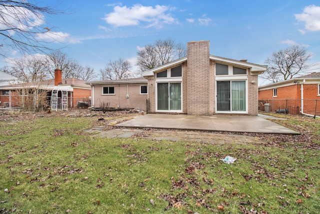 back of house featuring a patio area, brick siding, a chimney, and a lawn