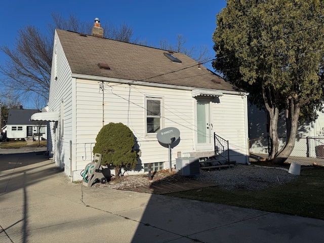 view of front of house featuring entry steps, a shingled roof, central AC unit, a chimney, and fence