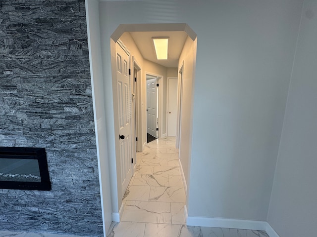 corridor with arched walkways, marble finish floor, and baseboards