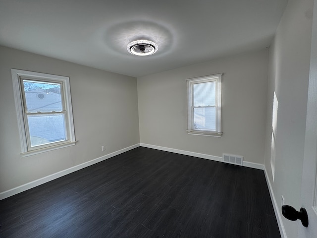 spare room with dark wood-style floors, visible vents, and baseboards