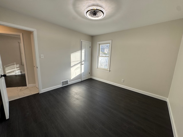 spare room with dark wood-style floors, visible vents, and baseboards