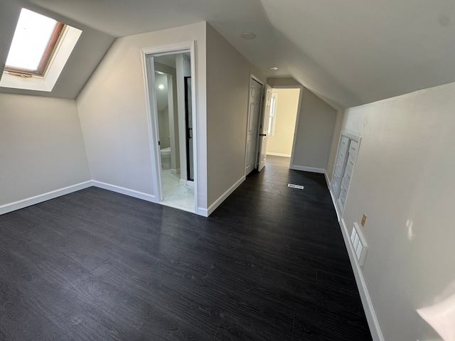 bonus room featuring vaulted ceiling with skylight, visible vents, dark wood finished floors, and baseboards