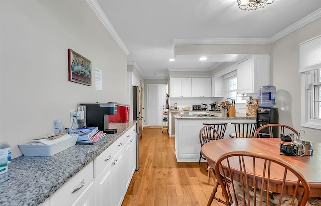 kitchen featuring light stone counters, a peninsula, white cabinets, ornamental molding, and light wood finished floors