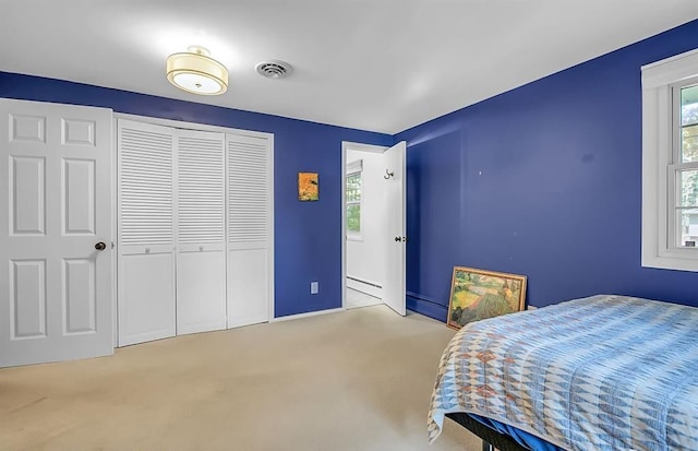 carpeted bedroom with multiple windows, baseboard heating, a closet, and visible vents