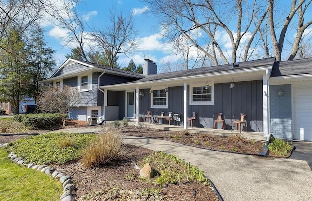 tri-level home with covered porch, brick siding, driveway, board and batten siding, and a chimney