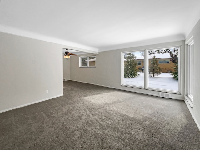 spare room with dark colored carpet, a ceiling fan, visible vents, and baseboards