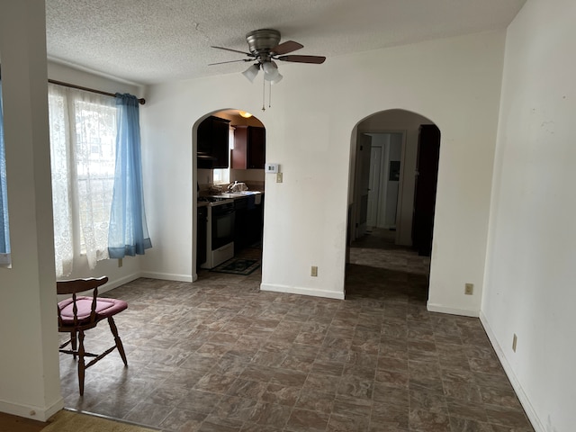 unfurnished room with arched walkways, ceiling fan, a textured ceiling, and a sink